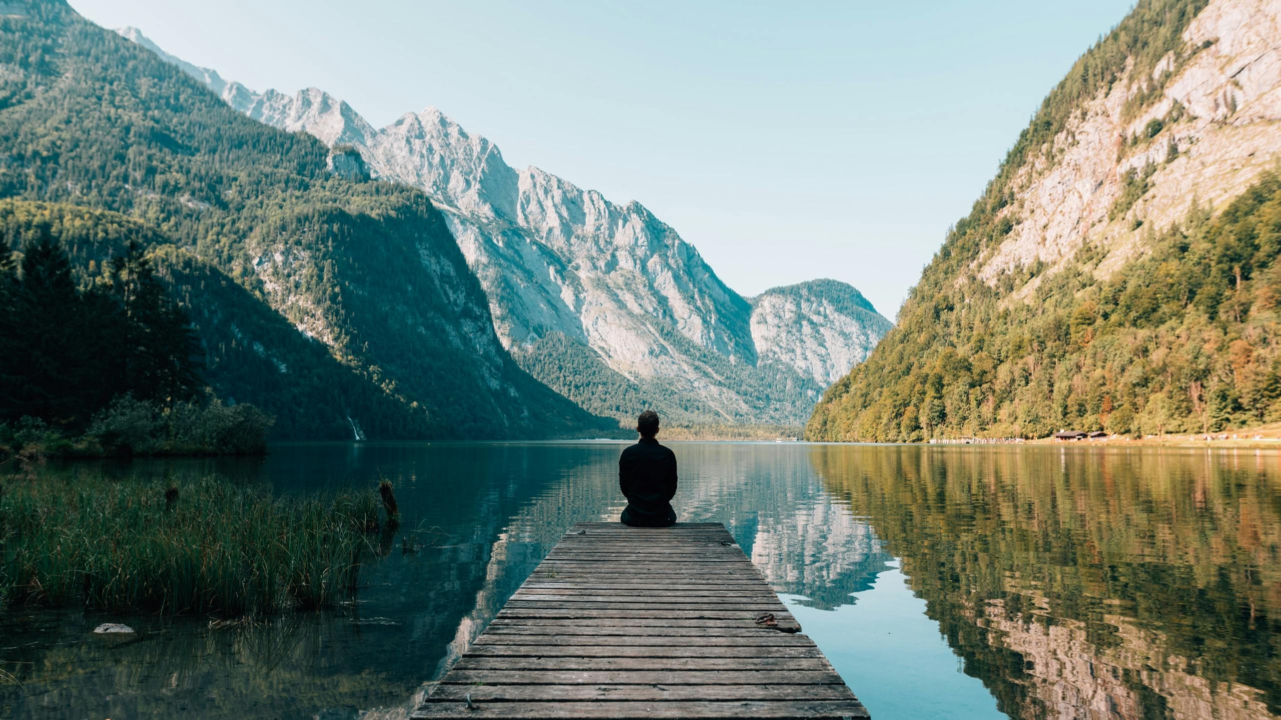 Man meditating while seated overlooking lake in mountainous region