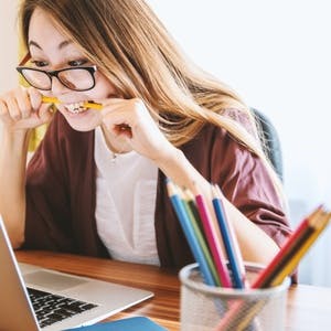 Woman biting pencil while staring at laptop