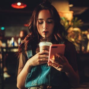 Woman staring at phone while drinking coffee